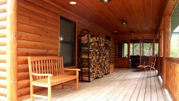 A wooden cabin with a porch, a bench, and a stack of firewood. - Luxury Lakefront Retreat on a Quiet Lake (Spooner)