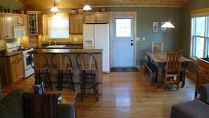 A kitchen with wooden cabinets, a refrigerator, a microwave, and a dining area with a table and chairs. - Luxury Lakefront Retreat on a Quiet Lake (Spooner)