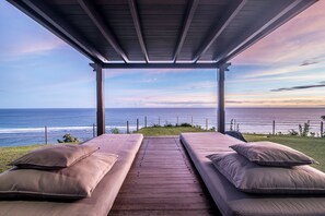 A covered outdoor seating area with two cushioned benches and a view of the ocean. - PANDAWA BEACH CLIFF EDGE ABSOLUTE OCEAN VIEW VILLA BALI 5 STAR LUXURY 3 BEDROOMS (kutuh)