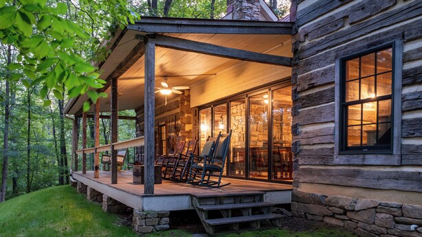 A log cabin with a porch, stone walls, and a glass door leading inside. - Restored Double Log Cabin on 400 Mountain Acres (Covesville)