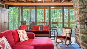 A cozy room with a red sofa, a rocking chair, and a stone wall. - Restored Double Log Cabin on 400 Mountain Acres (Covesville)