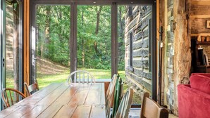 Una mesa de madera para comer con sillas, un sofá rojo y vistas a un bosque a través de amplias ventanas.