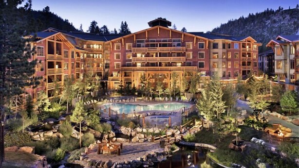 A large resort with multiple buildings, a central pool, and surrounding natural scenery.