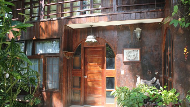 Une maison en bois avec une grande porte d’entrée, un balcon et un luminaire suspendu.