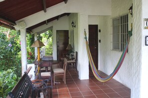 Un porche cubierto con una hamaca, muebles de madera y piso de baldosas.
