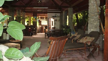 A covered outdoor seating area with a wooden chair and a cushioned lounge chair.