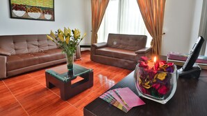 A living room with a brown leather sofa, a glass coffee table, and a vase with flowers. There is a desk with a lamp and a stack of magazines. - Casablanca Hotel, RestoBar, Catering, Events & Tourism in Garzón (Garzón)
