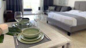 Ein ordentlich gedeckter Esstisch mit Tellern, Gläsern und einer Kerze, ein Bett und Blick ins Freie.