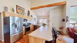 Una cocina con una isla grande, armarios de madera, electrodomésticos de acero inoxidable y un comedor con una silla roja.