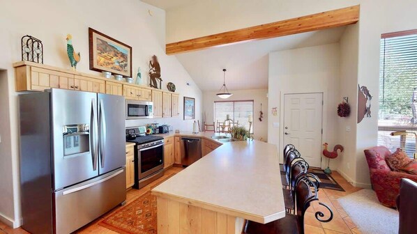 A kitchen with a large island, wooden cabinets, stainless steel appliances, and a dining area with a red chair.