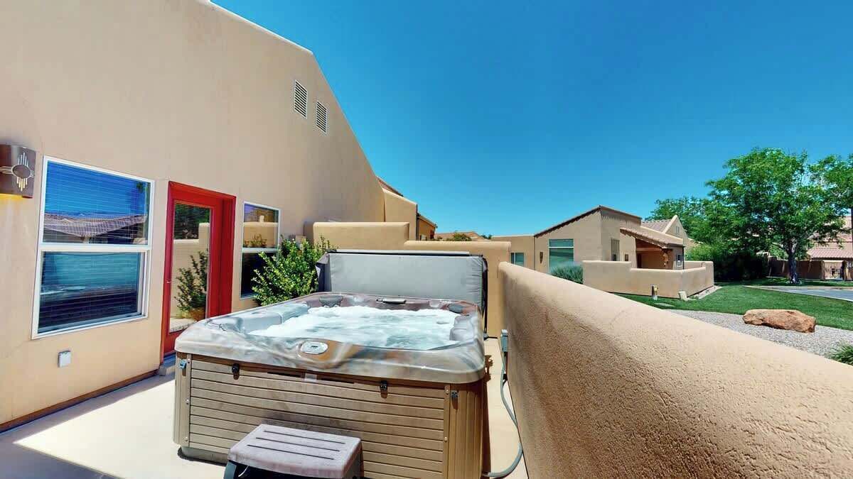 A hot tub on a balcony with a view of a house and a clear sky.