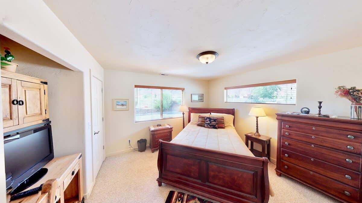 A bedroom with a bed, dresser, TV, and windows.
