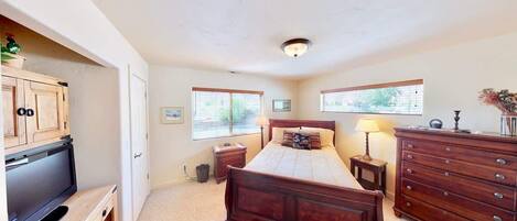 A bedroom with a bed, dresser, TV, and windows.