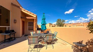 An outdoor patio with a table and chairs, a grill, and a blue umbrella.