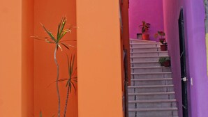 Un callejón estrecho con una escalera que lleva a una puerta, rodeado de paredes anaranjadas y moradas.