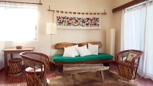 Una habitación con una cama de madera, dos sillones de mimbre, una mesita y un tapiz colorido en la pared.