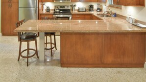 A kitchen with wooden cabinets, stainless steel appliances, a granite countertop, and two bar stools.