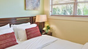 A neatly made bed with white and red pillows, a bedside lamp, and a small potted plant.
