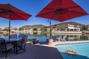 A poolside area with red umbrellas, lounge chairs, and a view of a lake and hills.