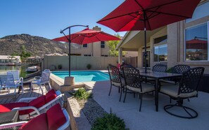 A poolside area with red umbrellas, lounge chairs, and a table with chairs.