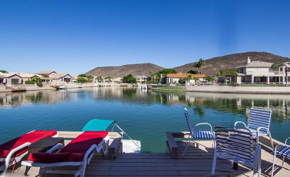 A waterfront property with a dock, lounge chairs, and a pool.