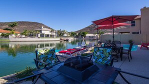 Un área junto a la piscina con sillones, una mesa y una sombrilla roja.