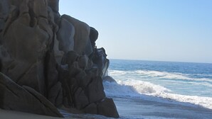 Una playa con un acantilado rocoso y olas rompiendo en la orilla.