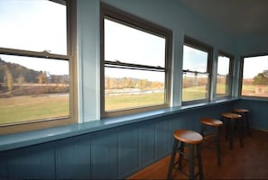 Una habitación con ventanas amplias, suelo de madera y tres taburetes de bar.