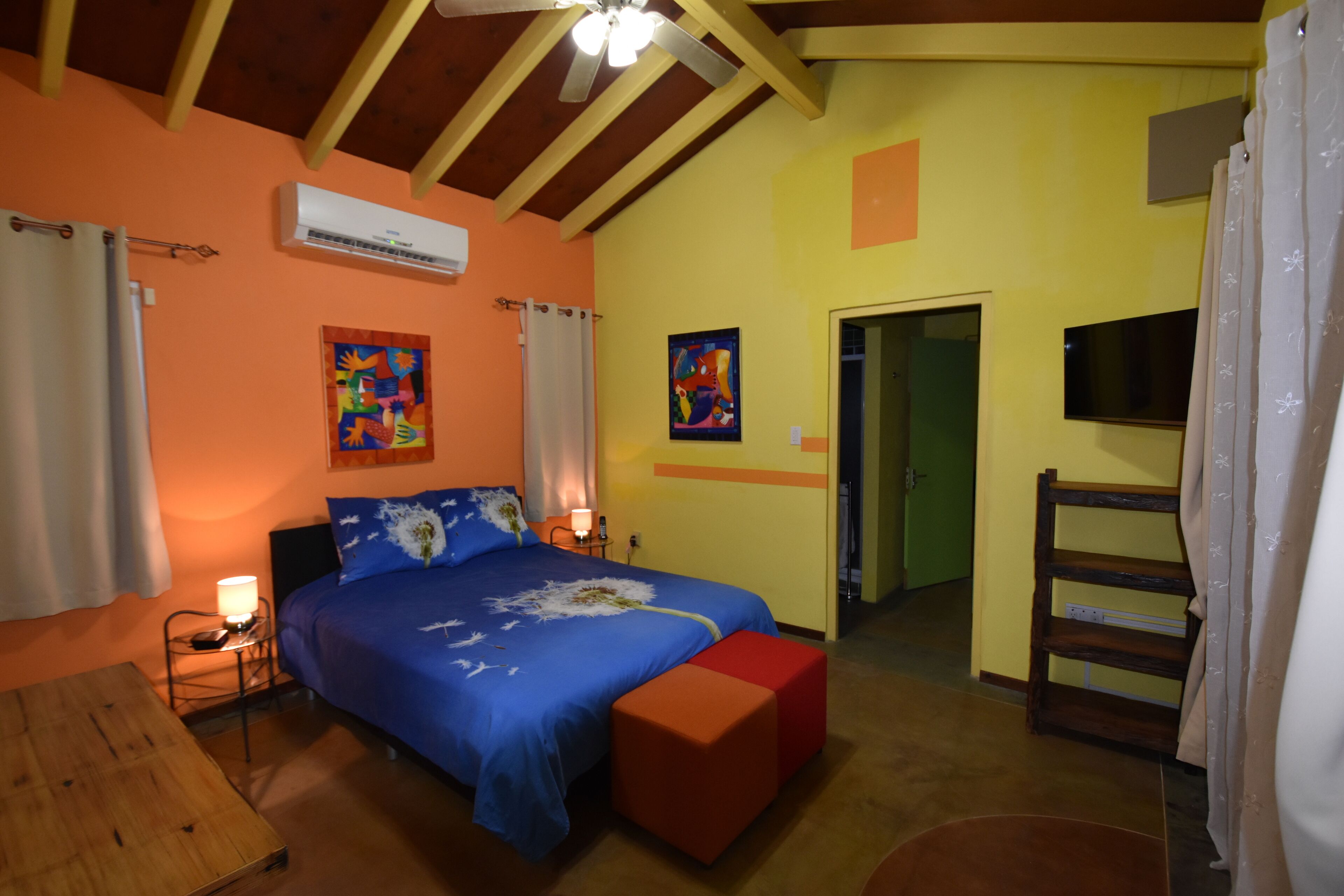 Un dormitorio con cama, mesitas de noche, aire acondicionado, televisor y un banco de madera.
