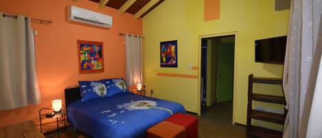 Un dormitorio con cama, mesitas de noche, aire acondicionado, televisor y un banco de madera.