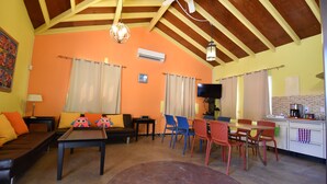 Ein Wohnzimmer mit Sofa, Couchtisch und Stühlen, ein Essbereich mit Tisch und Stühlen sowie eine Küche mit Arbeitsplatte und Geräten.