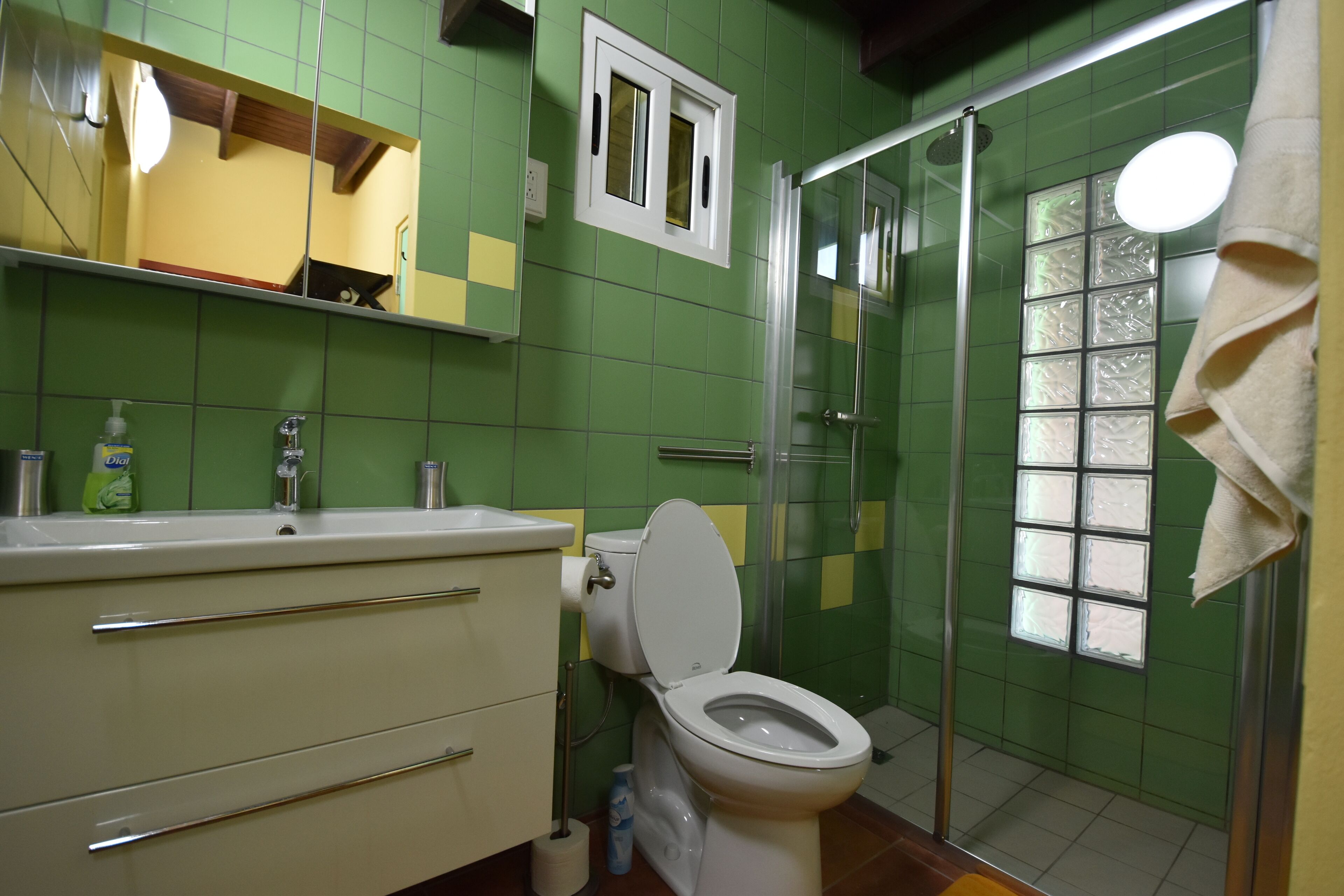 A bathroom with green tiles, a white toilet, a sink with a mirror, and a shower area.