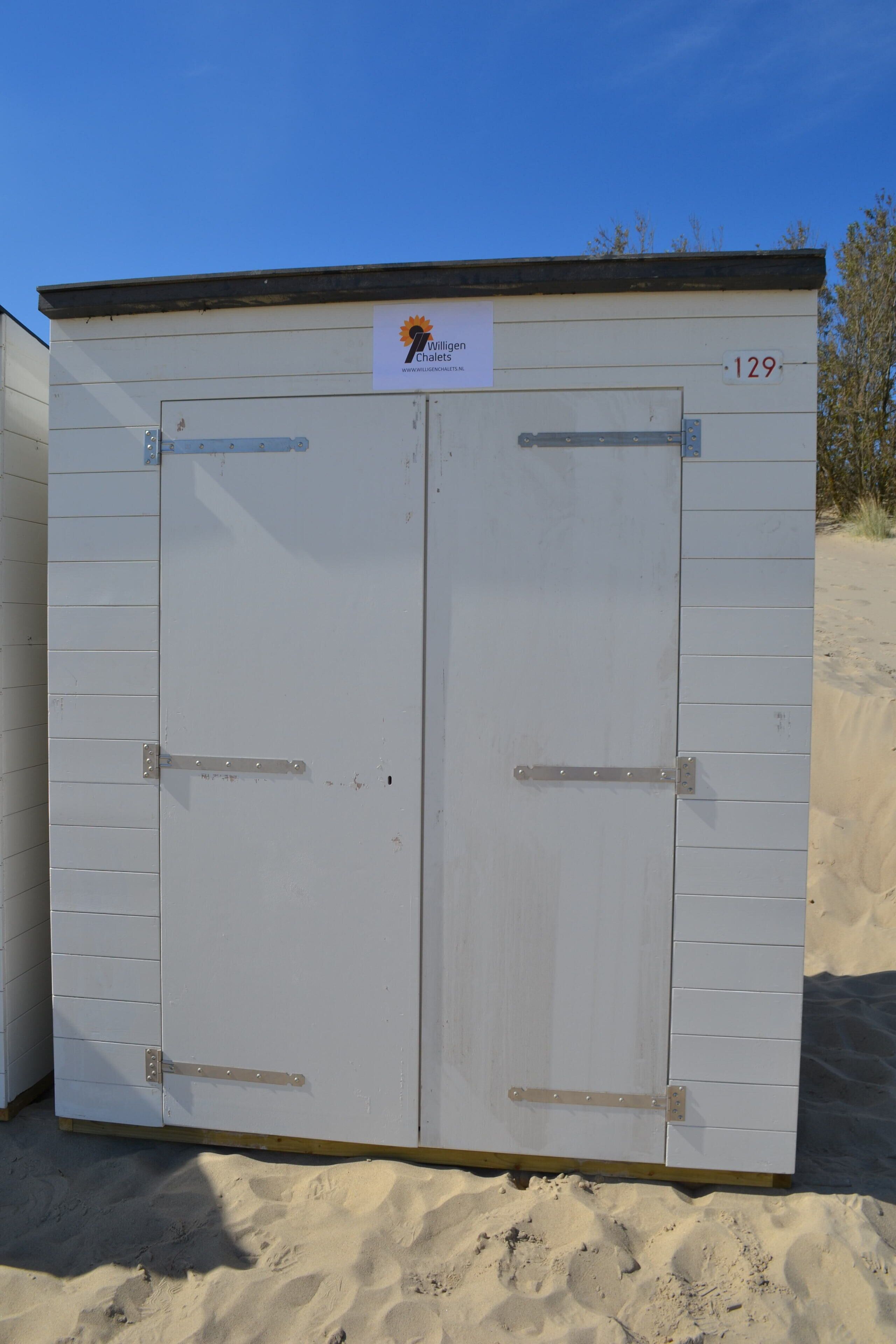 Een wit gebouw met twee deuren, een bord met een logo en het nummer 129.