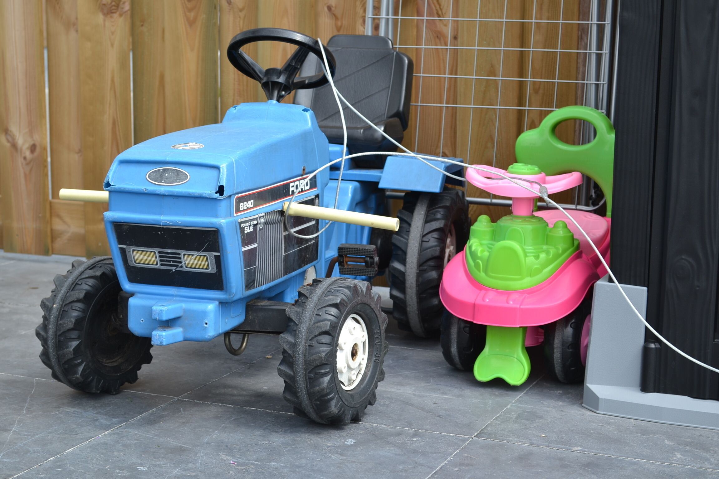 A blue toy tractor with a steering wheel and a green and pink toy vehicle.