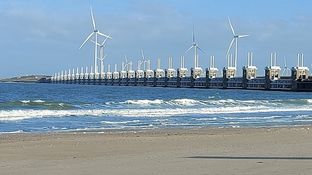 Vista costera con un muelle largo que se adentra en el mar, con varias turbinas eólicas.