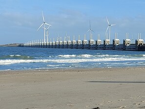 Vista costera con un muelle largo que se adentra en el mar, con varias turbinas eólicas.