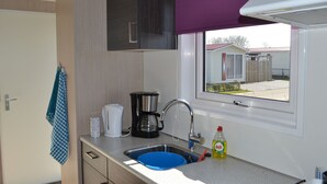 Una kitchenette compacta con pileta integrada, cafetera y ventana con vista a un barrio residencial.