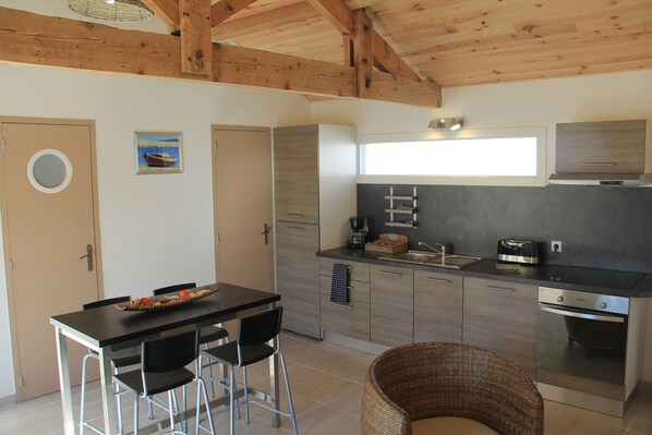 A modern kitchen with a dining area, featuring a wooden ceiling, a black countertop, and stainless steel appliances. - SPECIAL OFFER: Traditional cottage in the Arcachon Bay area near the port of Audenge (Audenge)