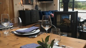 A dining table set with plates, glasses, and cutlery, with a view of a living area and a fireplace in the background. - Luxury Holiday Home with Hot Tub,  Pet & Family friendly in the Yorkshire Dales  (Eastby)