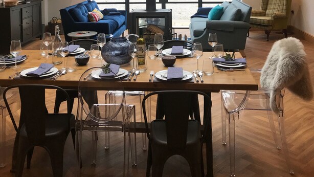 A modern dining area with a high ceiling, large windows, and a central wood-burning stove. - Luxury Holiday Home with Hot Tub,  Pet & Family friendly in the Yorkshire Dales  (Eastby)