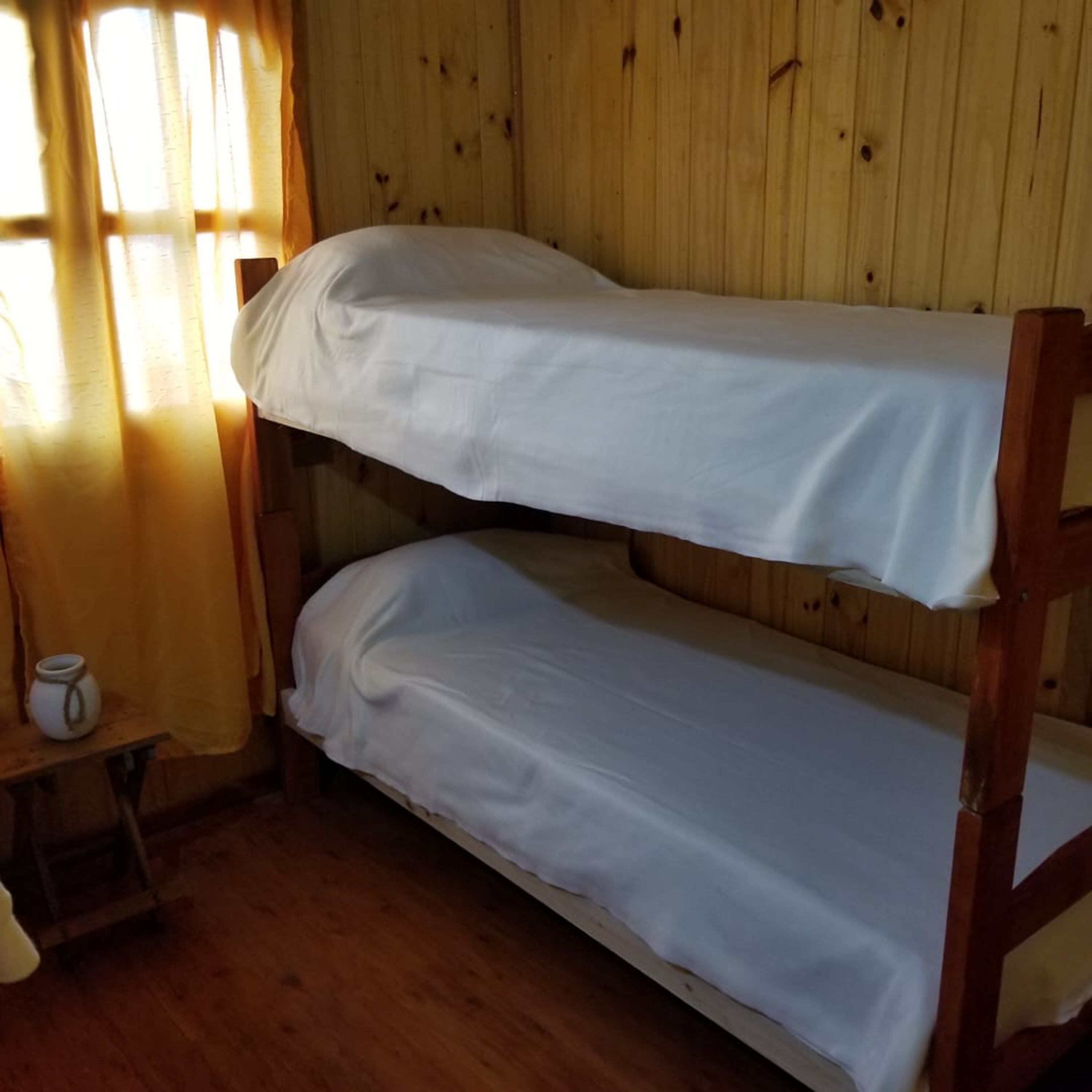 Una cama litera en una habitación con paredes de madera y una ventana con cortinas.