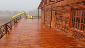 A wooden deck with a metal railing, a play structure, and a log cabin building. - Mar de Sueños Parque Acuático Infantil (Parana)