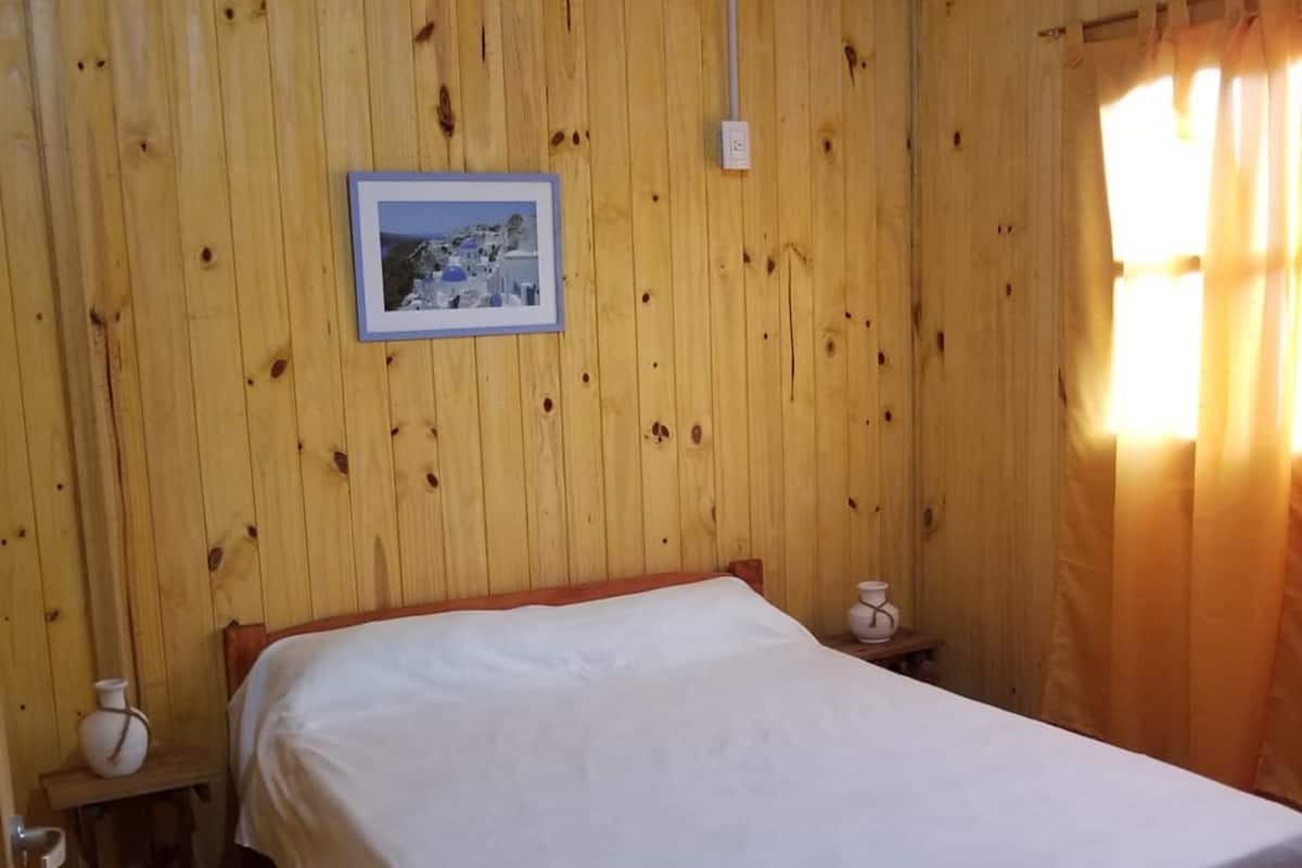 Une pièce en bois avec un lit, un tableau encadré au mur et une petite table sur laquelle se trouve un vase.