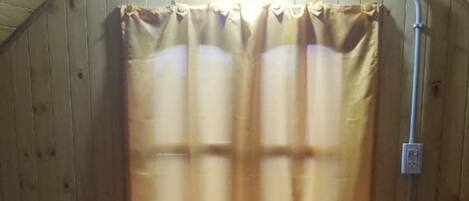 Habitación acogedora con paredes de madera y techo inclinado, que incluye dos camas con ropa de cama marrón, una mesita con una lámpara y una ventana con cortinas.