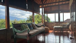 Una terraza de madera con un sofá y una silla de mimbre, con vistas a un paisaje montañoso.