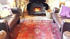 A cozy living room with a stone fireplace, leather sofas, and a patterned rug. - Outstanding Self Catering Cottage With Beautiful Gardens (Albourne)