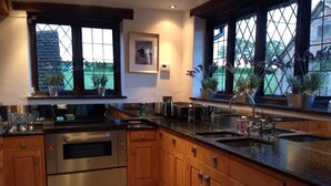 A modern kitchen with stainless steel appliances, wooden cabinets, and large windows overlooking a garden. - Outstanding Self Catering Cottage With Beautiful Gardens (Albourne)