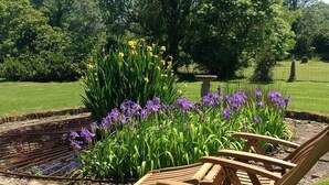 A garden with a circular flower bed, wooden chairs, and a stone fountain. - Outstanding Self Catering Cottage With Beautiful Gardens (Albourne)
