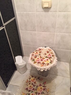 A bathroom with a toilet, a tissue box, and a floral-patterned rug.