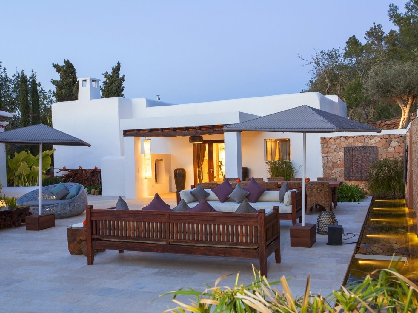 A modern outdoor living area with a wooden bench, a covered seating area, and a stone wall.